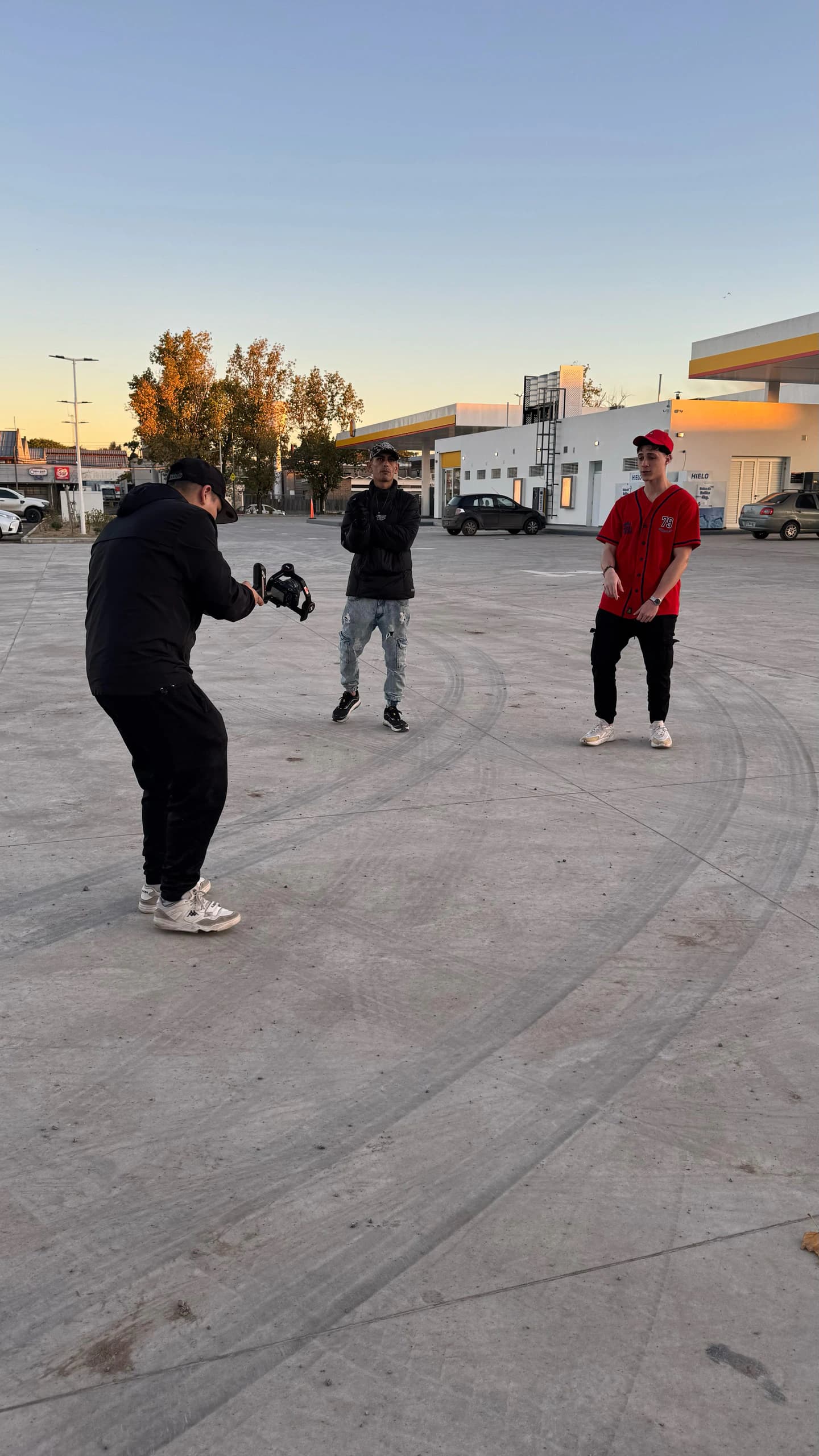 Brian filmando cámara en mano a dos artistas en una estación de servicio, al atardecer