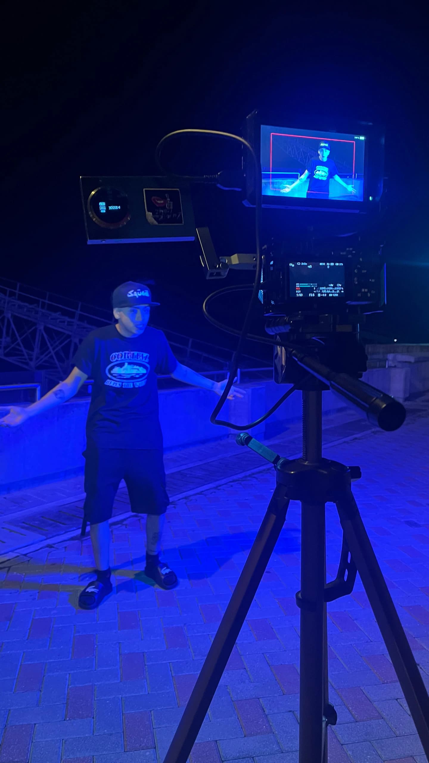 Cámara en trípode con monitor externo encuadrando a un artista en un rodaje de noche