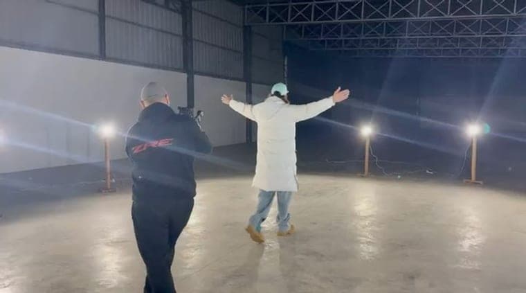 Brian filma con gimbal a un artista de campera blanca en un galpón, entre luces sobre pedestales y humo